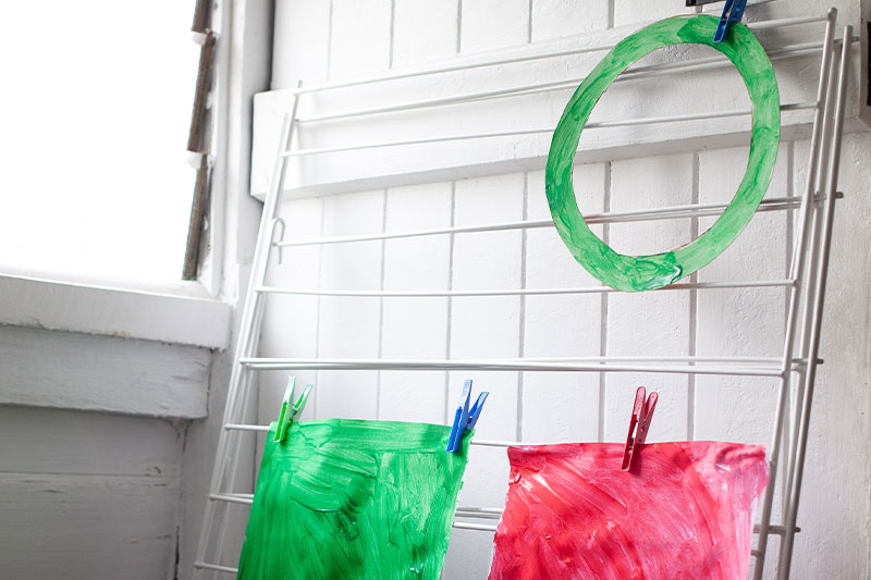 Painted paper wreath and craft materials drying on a clothes rack.