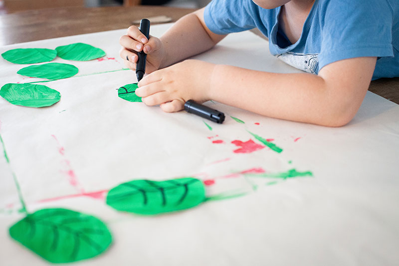 Child creating green paper leaves for a handmade remembrance poppy wreath activity.