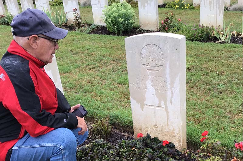 Visitor paying respects beside a Commonwealth War Graves headstone in a military cemetery.