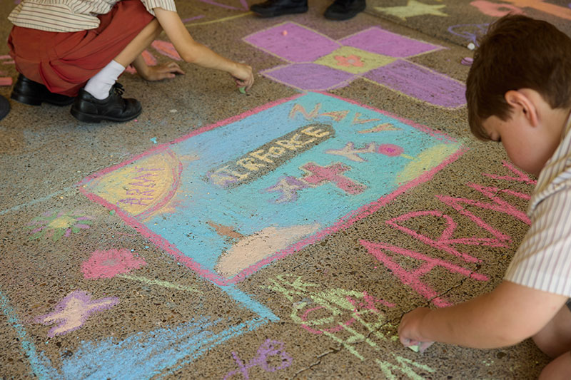 Students drawing remembrance-themed chalk art featuring a military vehicle and commemorative symbols.