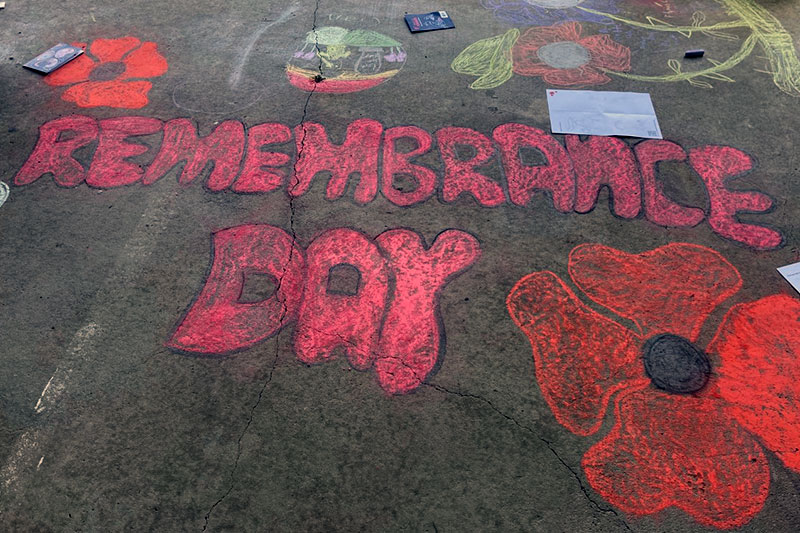 Chalk artwork displaying the words “Remembrance Day” alongside red poppies.