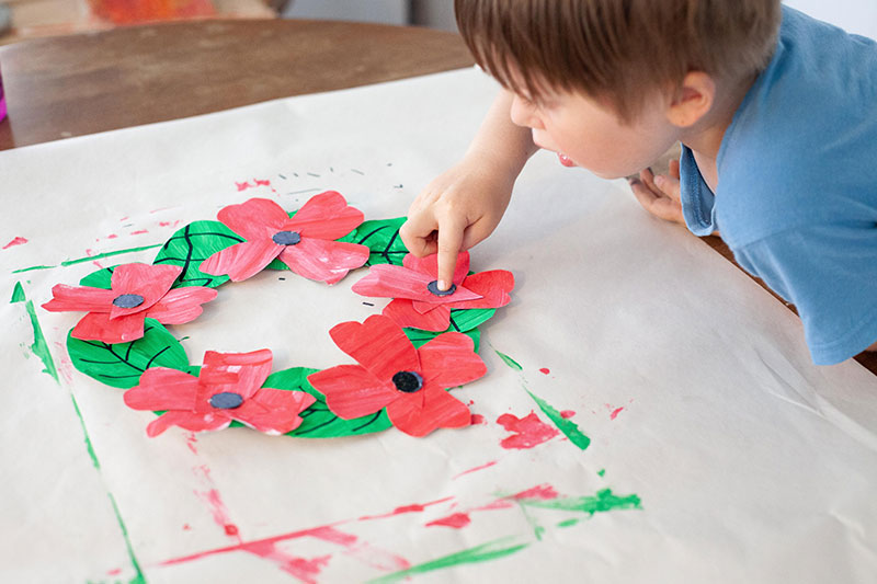 Child placing handmade paper poppies onto a remembrance wreath craft project.
