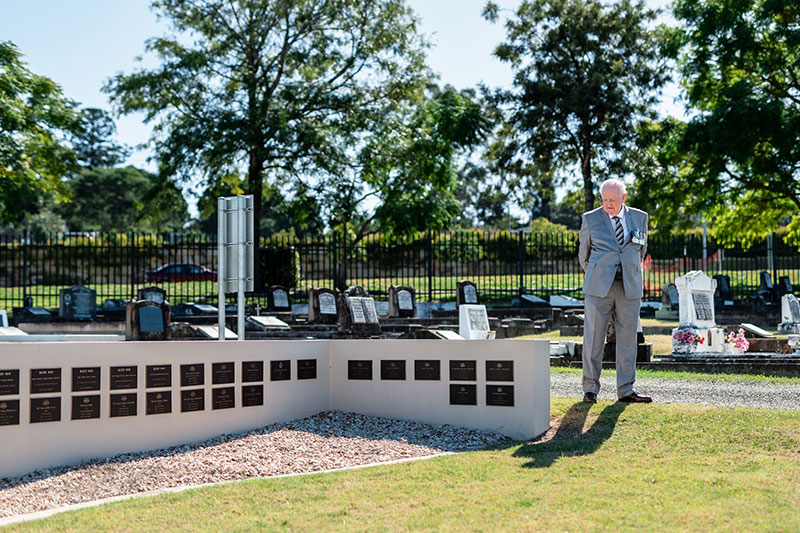Visitor standing beside a memorial wall displaying plaques commemorating Australian service personnel.